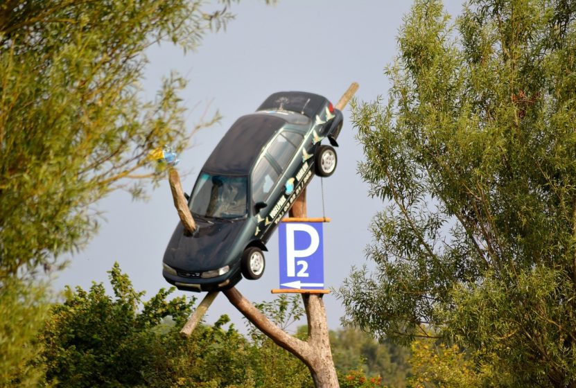 car hanging on a tree with a parking sign